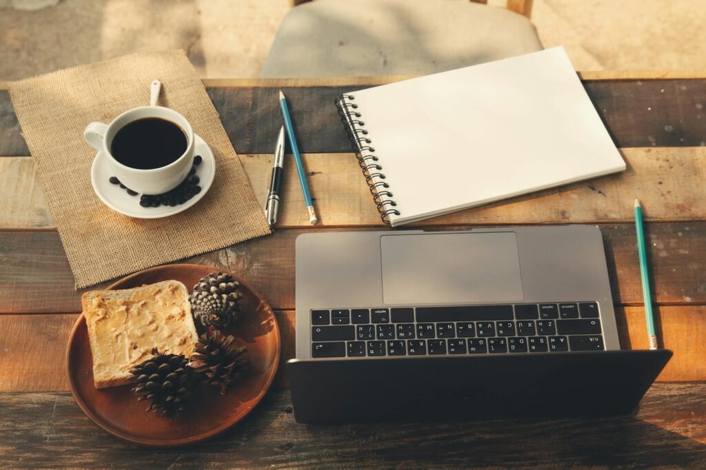 Flat lay of a writing desk with a laptop, notebook, pen, and coffee mug on a wooden surface
