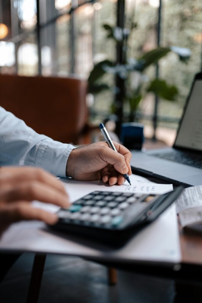 Stressed man using a calculator while working on a laptop