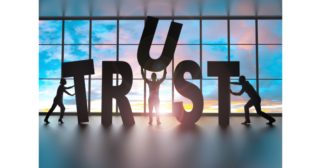 Silhouetted figures working together to hold up the word “TRUST” against a bright window.