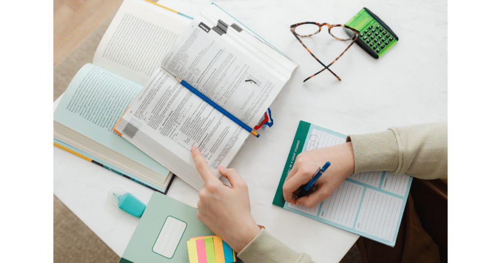Overhead view of an open notebook, scattered pens, and planner pages on a busy desk—organized chaos in the middle of a writing project.