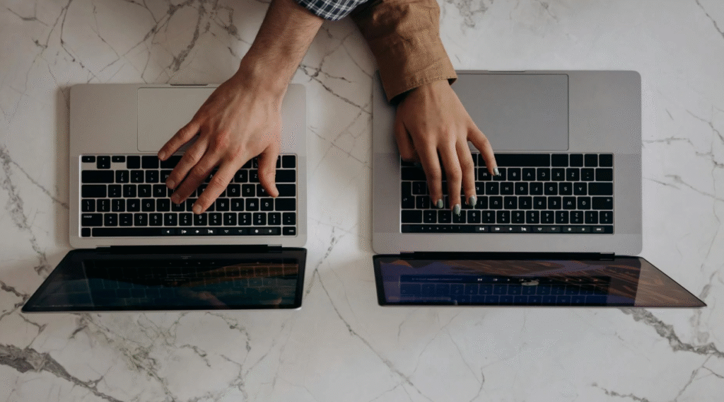 Two people working side by side on laptops at a shared desk, symbolizing collaborative editing and partnership.