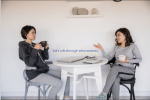 Two women talk over coffee at a small round table, reflecting the tone of a coaching fit call conversation.