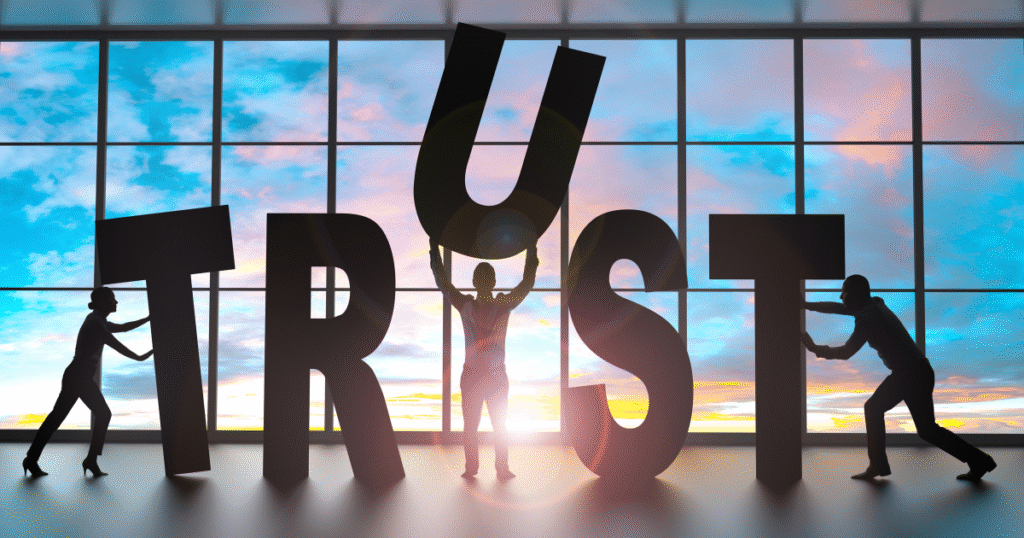 Silhouetted figures working together to hold up the word “TRUST” against a bright window.