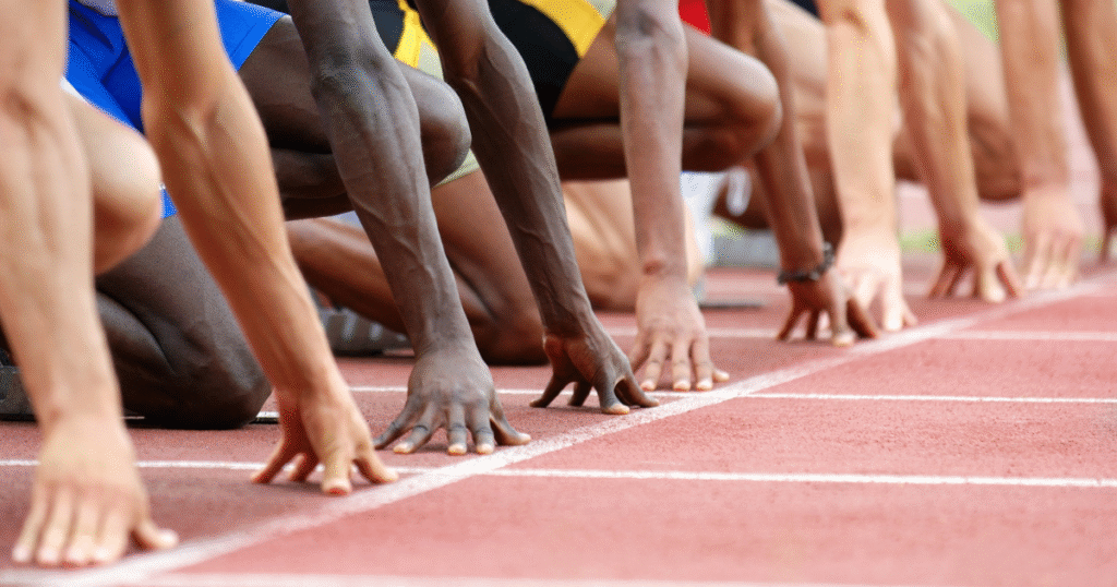 Close-up of sprinters' hands on the starting line, poised to launch from the blocks.