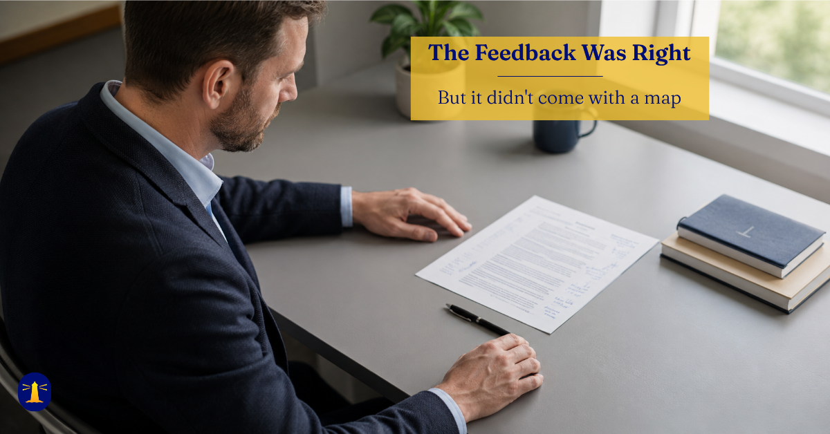 A business professional in a navy blazer sits at a desk, looking down at an annotated document. A pen rests on the table. He is not writing.